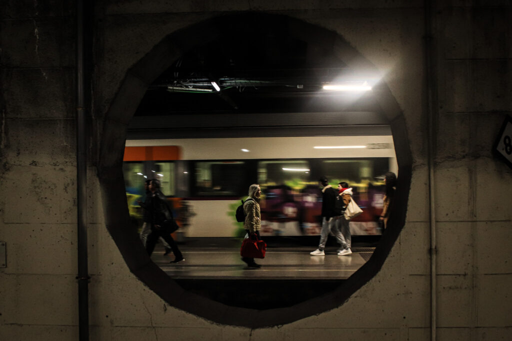 Interior d’un tren de Rodalies ple o andana amb gent en moviment 👉 Representa els desplaçaments quotidians entre municipis i la dependència metropolitana.