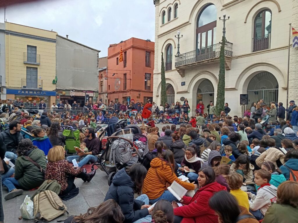 La plaça de la vila plena de gom a gom de nens i gent gran llegint asseguda a terra foto: Tomeu Ferrer